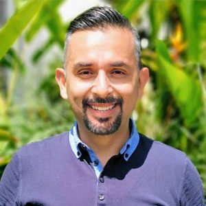 Mauricio smiling outside in front of plants and flowers