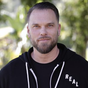 Adam smiling outside in a black and white hooded sweatshirt