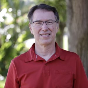 Dennis smiling outside in a red collared shirt