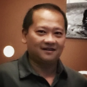 Daniel smiling with a brown wall and black and white picture in the background